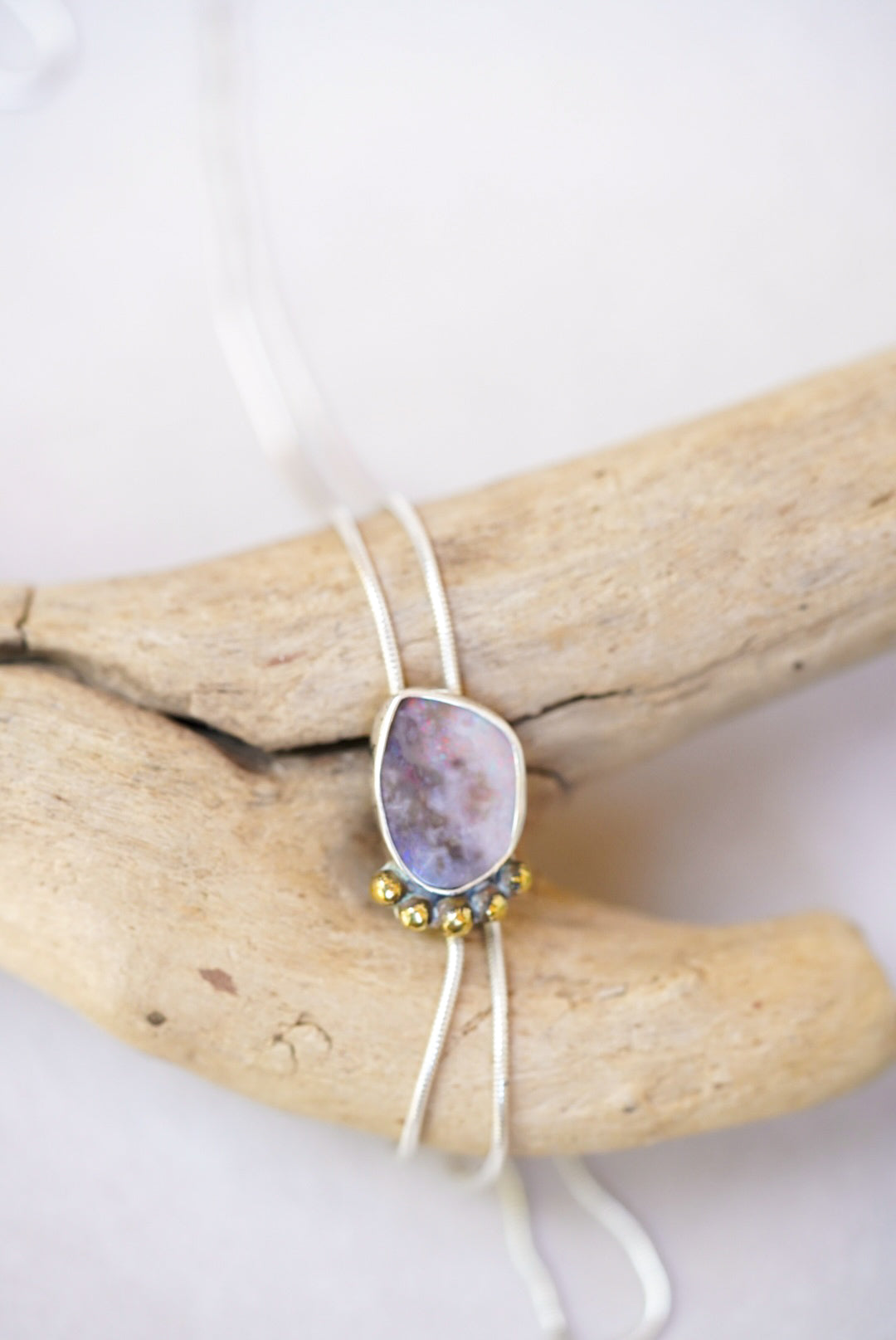 Opal bolo necklace on a piece of driftwood on a white background