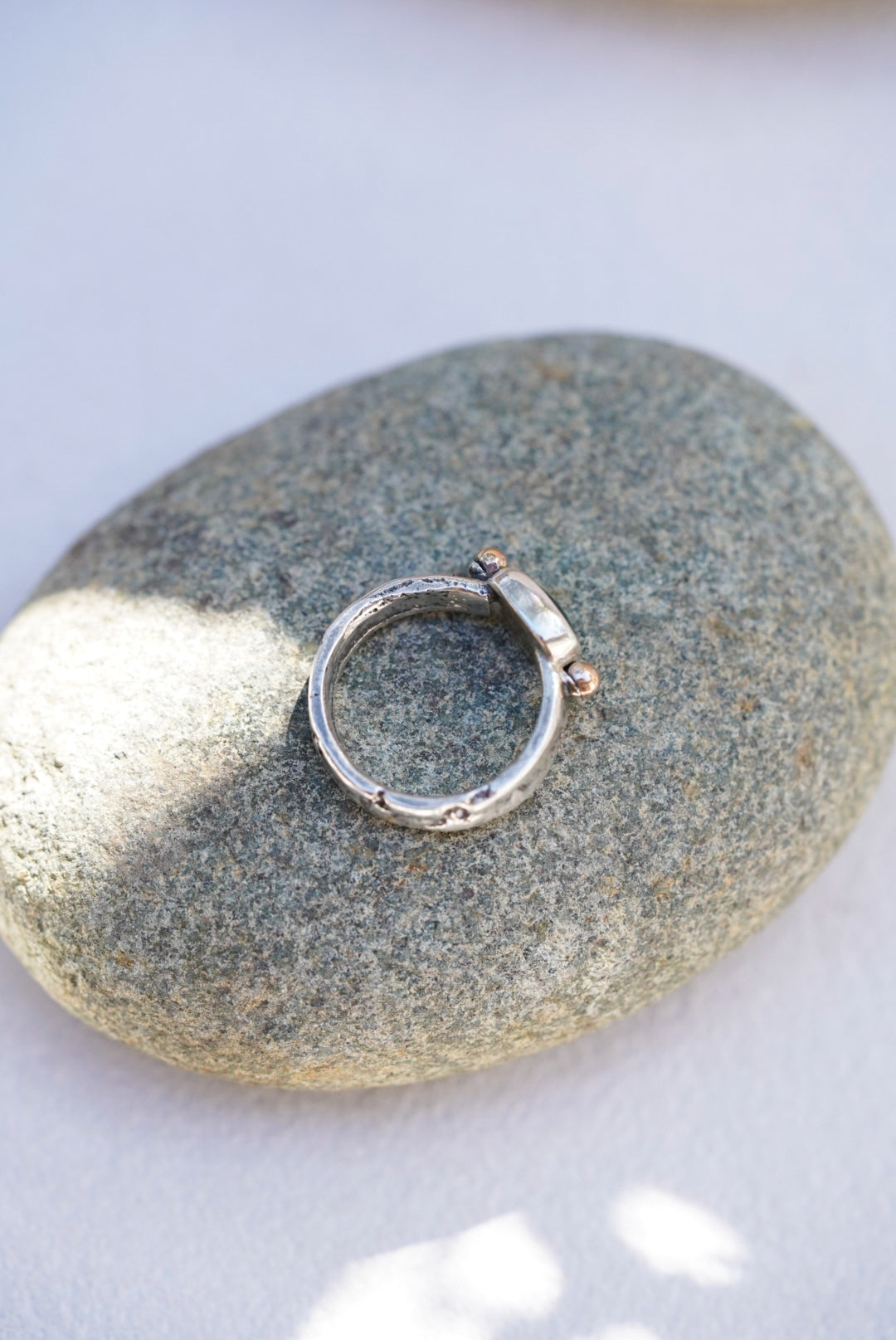 A silver ring with a rectangular kyanite gemstone on a smooth gray stone against a light background.