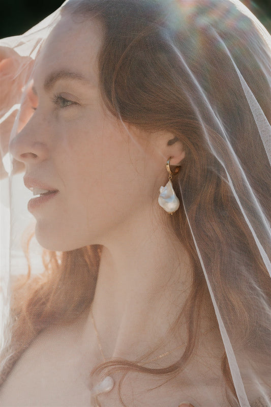 Woman wearing a veil with a soft, blurred background and pearl earring