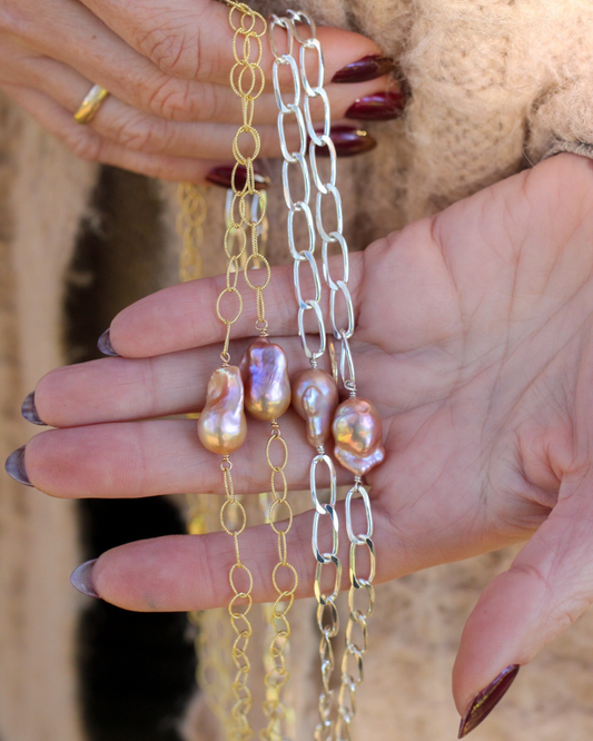 Two pearl necklaces in gold and silver held by a hand with dark nail polish.