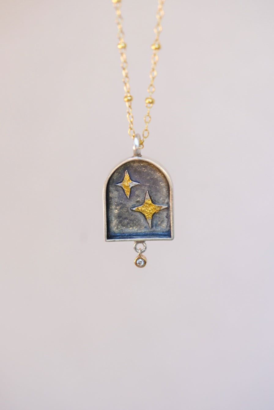 pendant with celestial design and a small diamond with a neutral background 