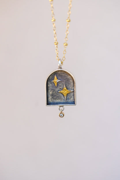 pendant with celestial design and a small diamond with a neutral background 