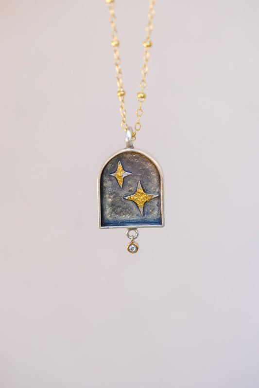 pendant with celestial design and a small diamond with a neutral background 