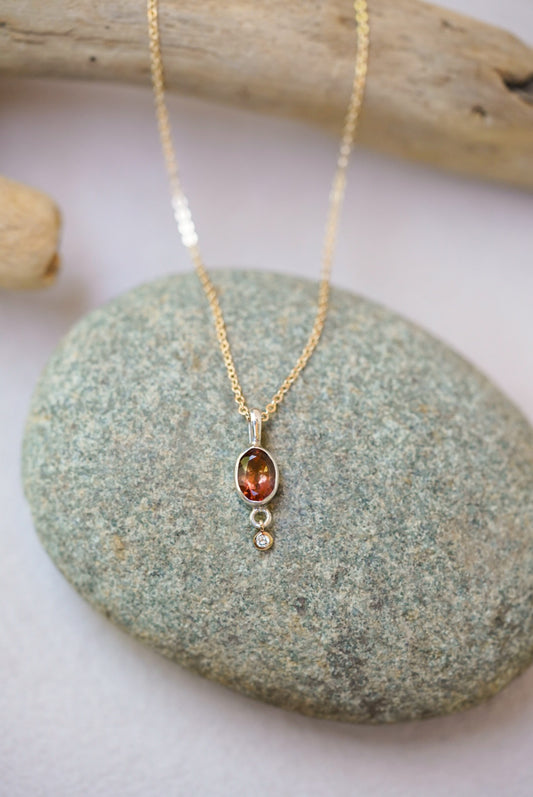 Tourmaline pendant necklace with a diamond dangling underneath, on top of a river rock