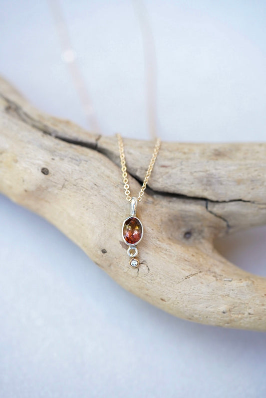 Tourmaline pendant necklace with a diamond dangling underneath, on top of a piece of driftwood