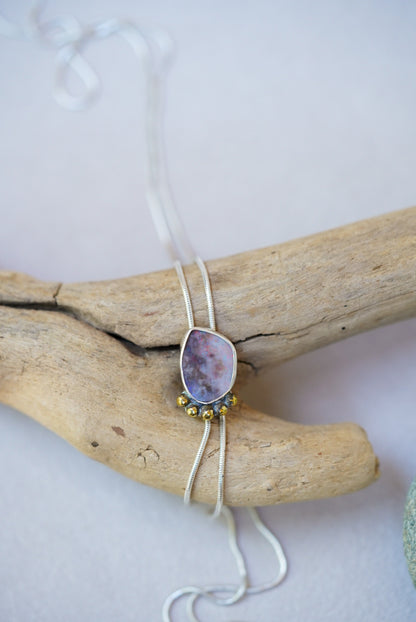 Opal bolo necklace on a piece of driftwood on a white background