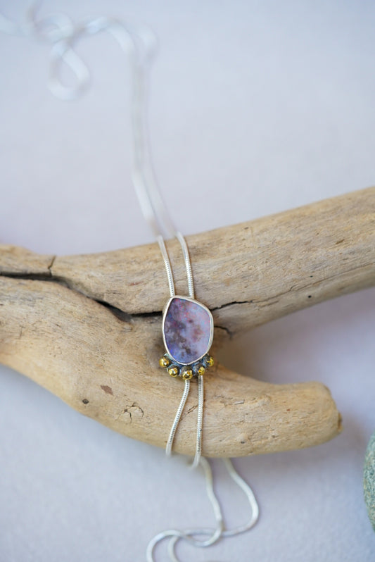 Opal bolo necklace on a piece of driftwood on a white background