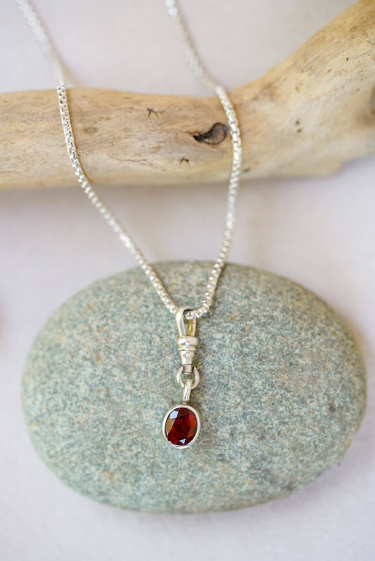 Silver necklace with a red gemstone pendant on a stone surface