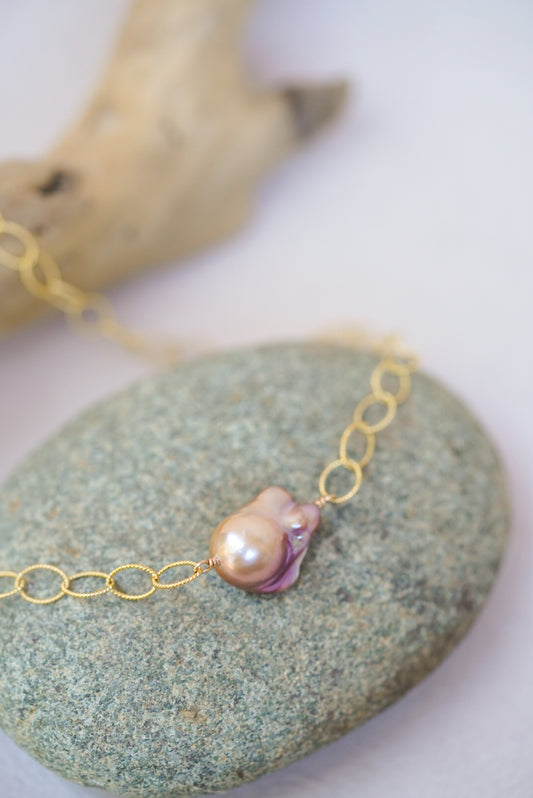 Gold chain necklace with a pink pearl on a stone surface