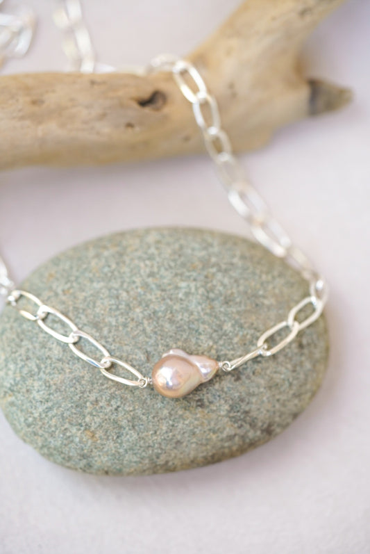 Silver chain necklace with a pearl pendant on a stone surface