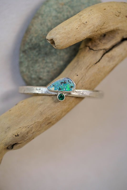 Silver cuff with a green gemstone on a piece of driftwood