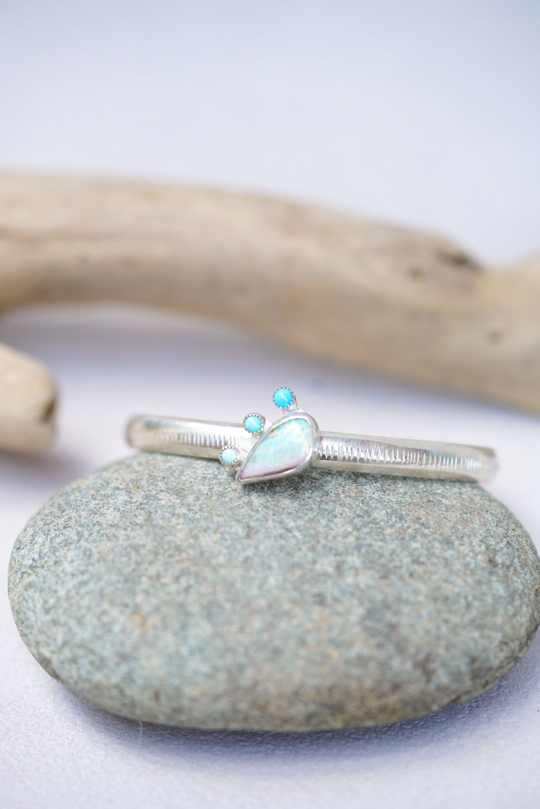 Silver cuff with turquoise and opal stones on a stone surface