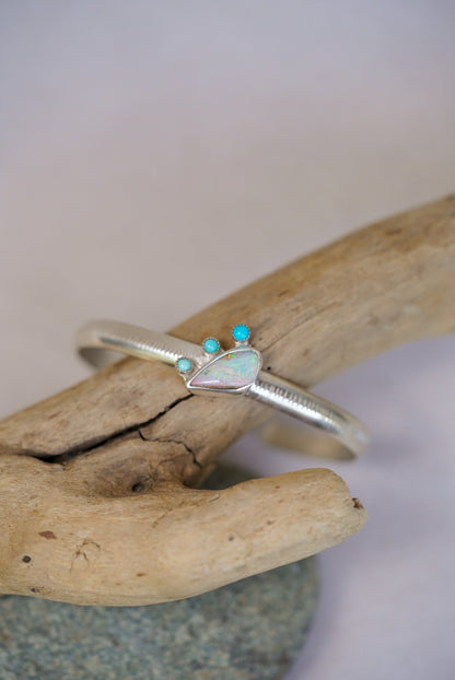 Silver cuff with opal and turquoise stones on a piece of driftwood