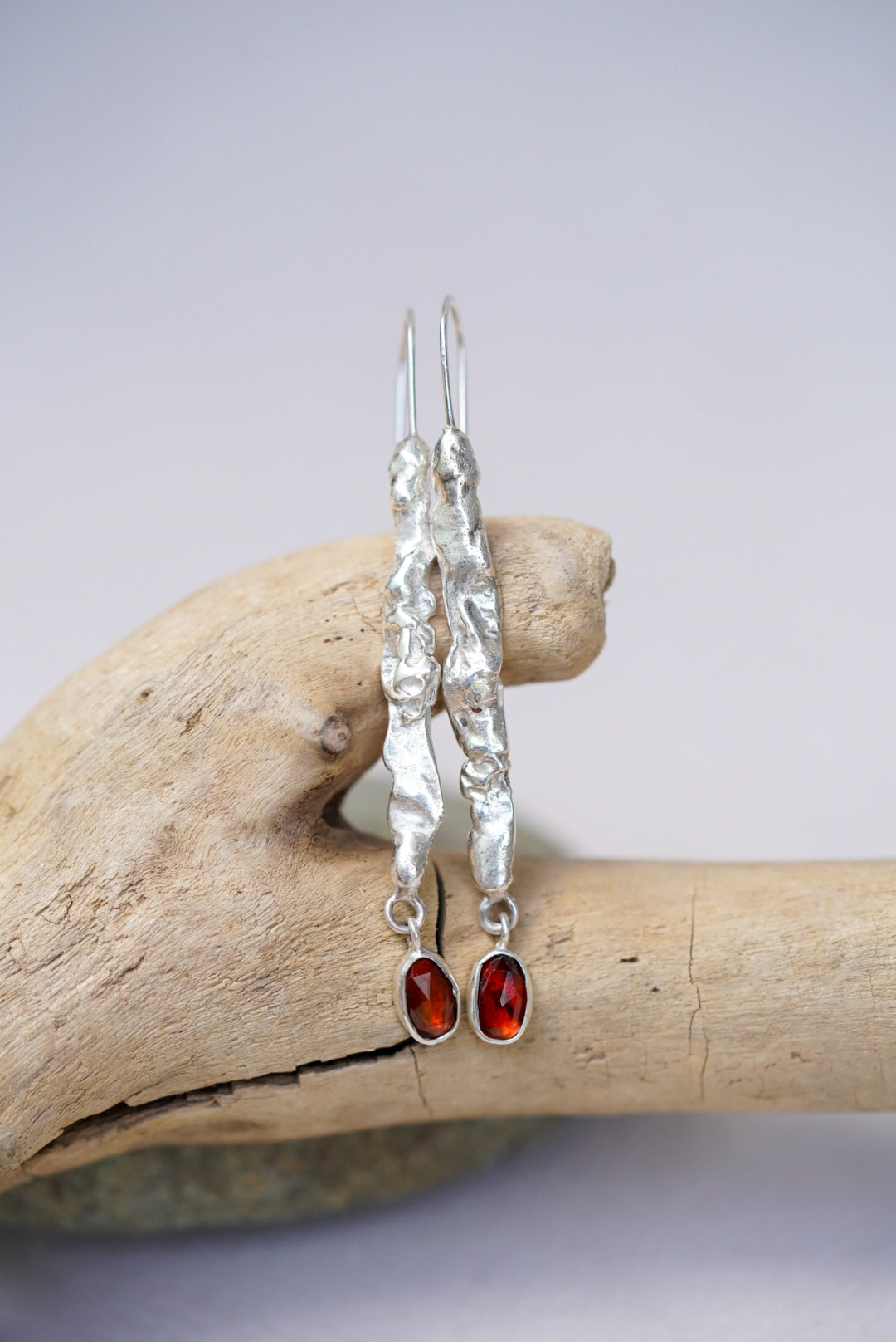 Silver earrings with garnet stones on a piece of driftwood against a light background