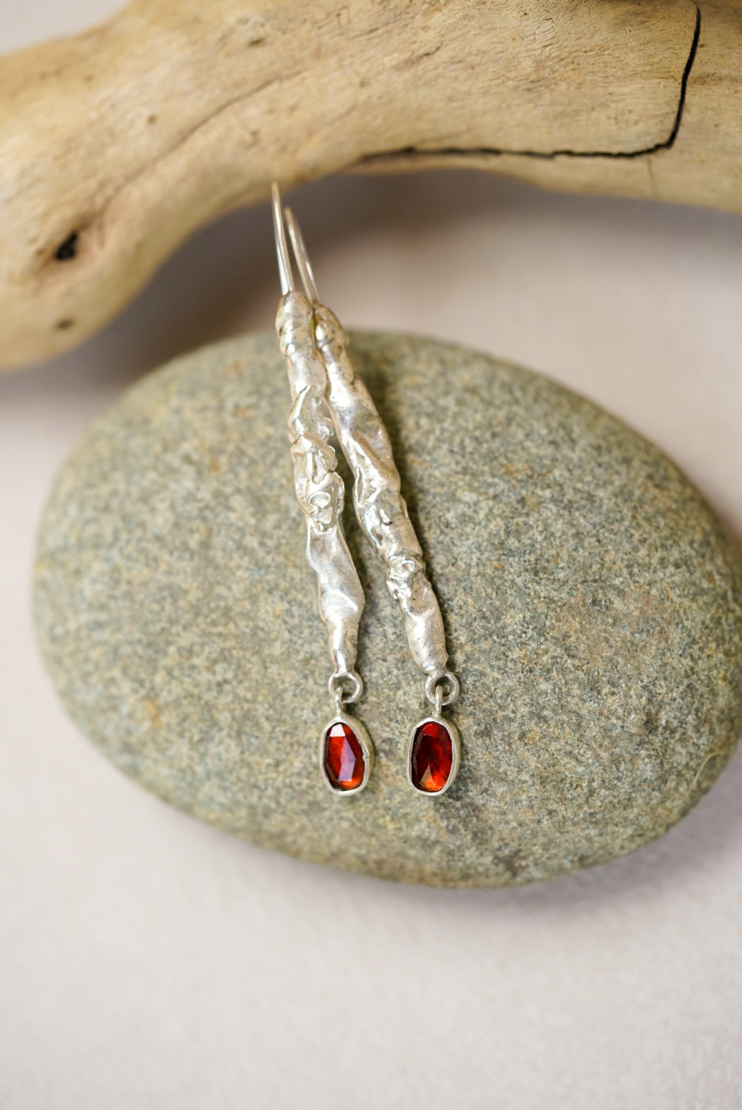 Silver earrings with red gemstones on a stone surface