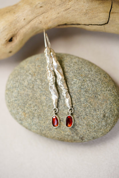 Silver earrings with red gemstones on a stone surface