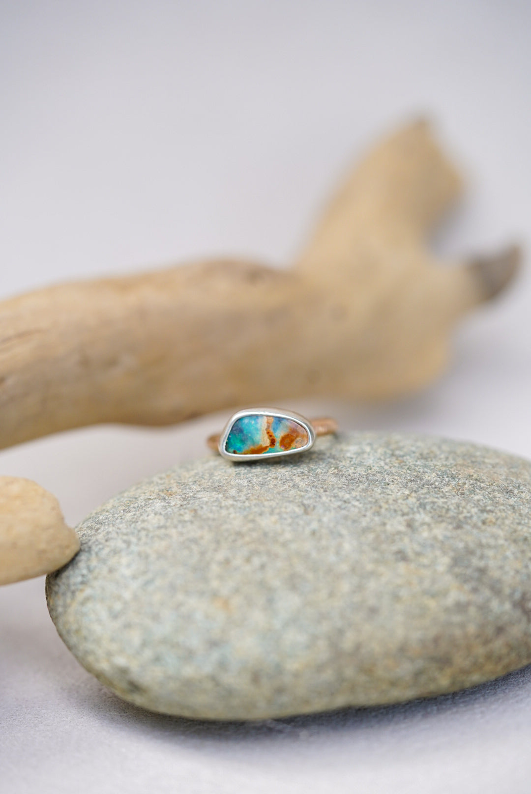 Ring with a colorful stone on a stone surface with driftwood in the background