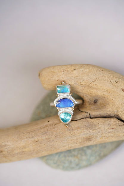 Silver ring with blue and green gemstones on a piece of driftwood.