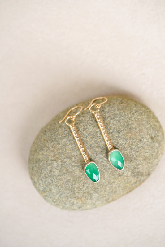 Gold earrings with green gemstones on a stone surface