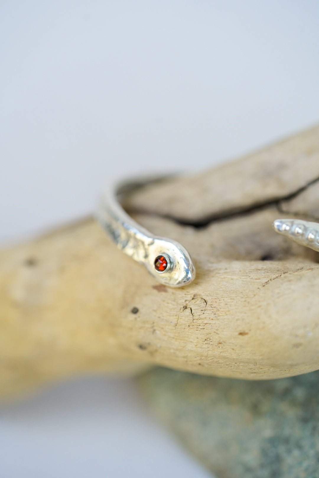 Silver cuff with a red stone on a piece of driftwood against a light background