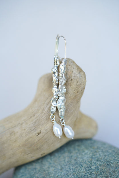 Silver earrings with pearls on a piece of driftwood against a light background