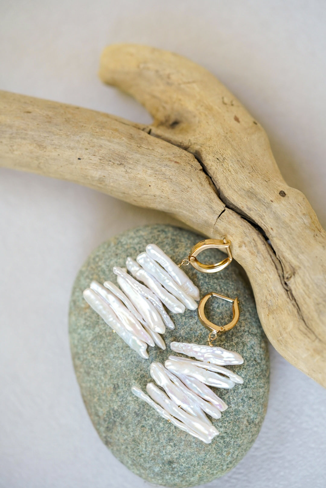 Gold and pearl earrings on a stone with driftwood