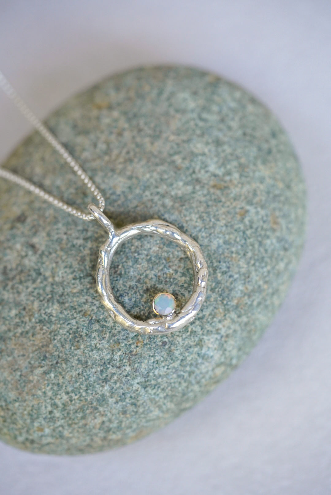 Silver necklace with a circular pendant on a textured stone surface