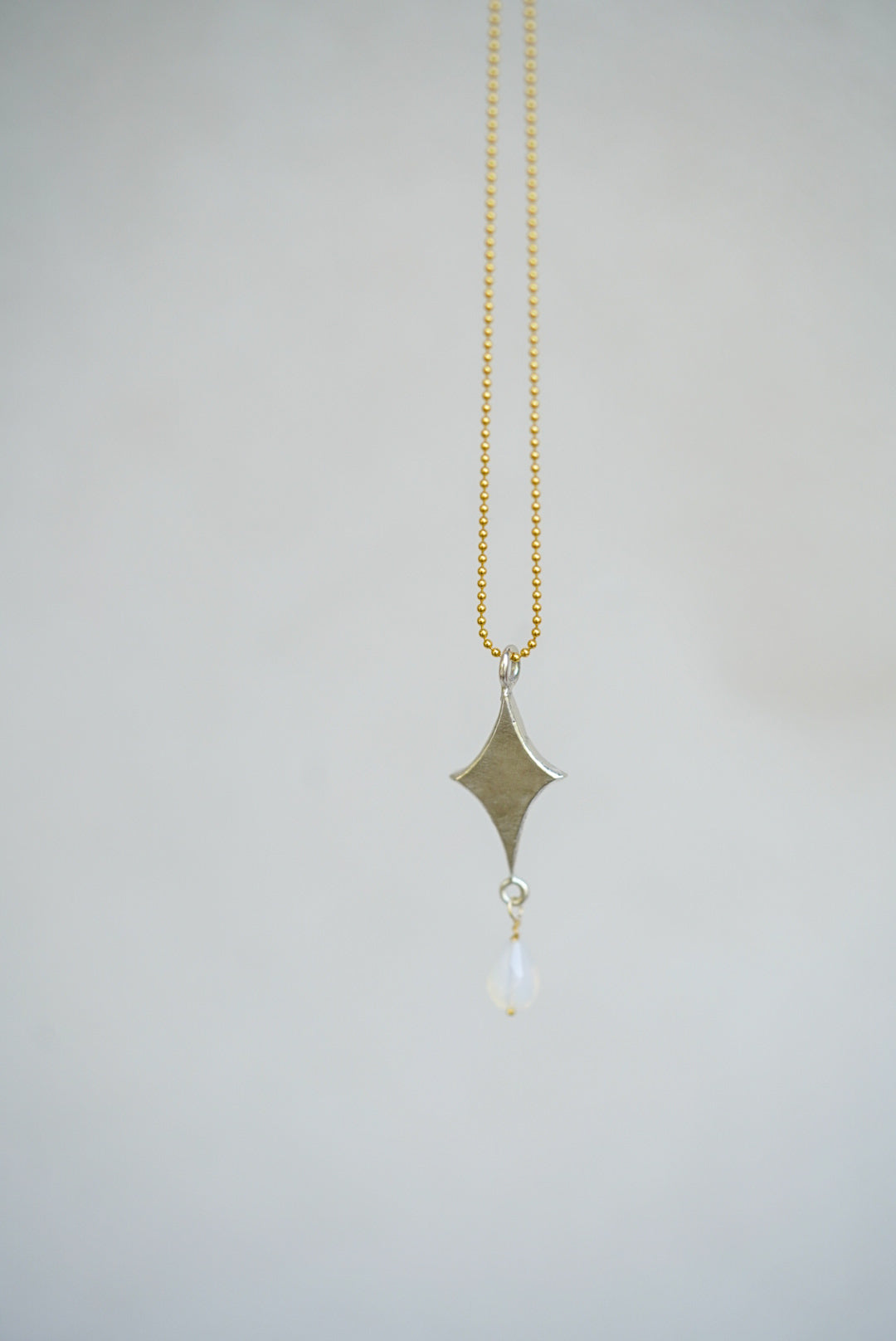 Necklace with a diamond-shaped pendant and gold chain on a light gray background