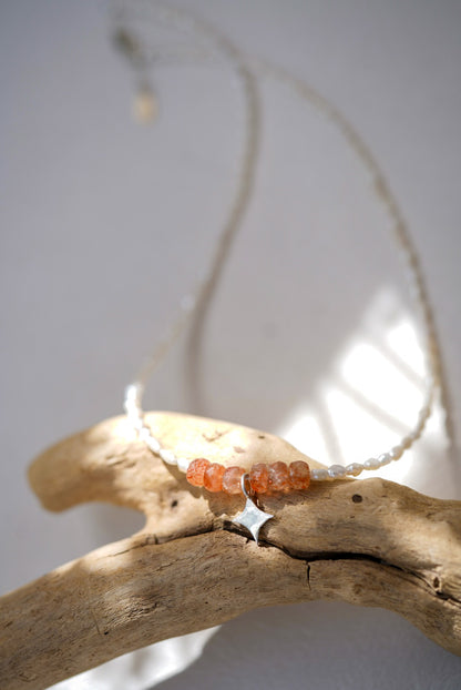 Necklace with sunstone and pearl beads on a branch against a light background