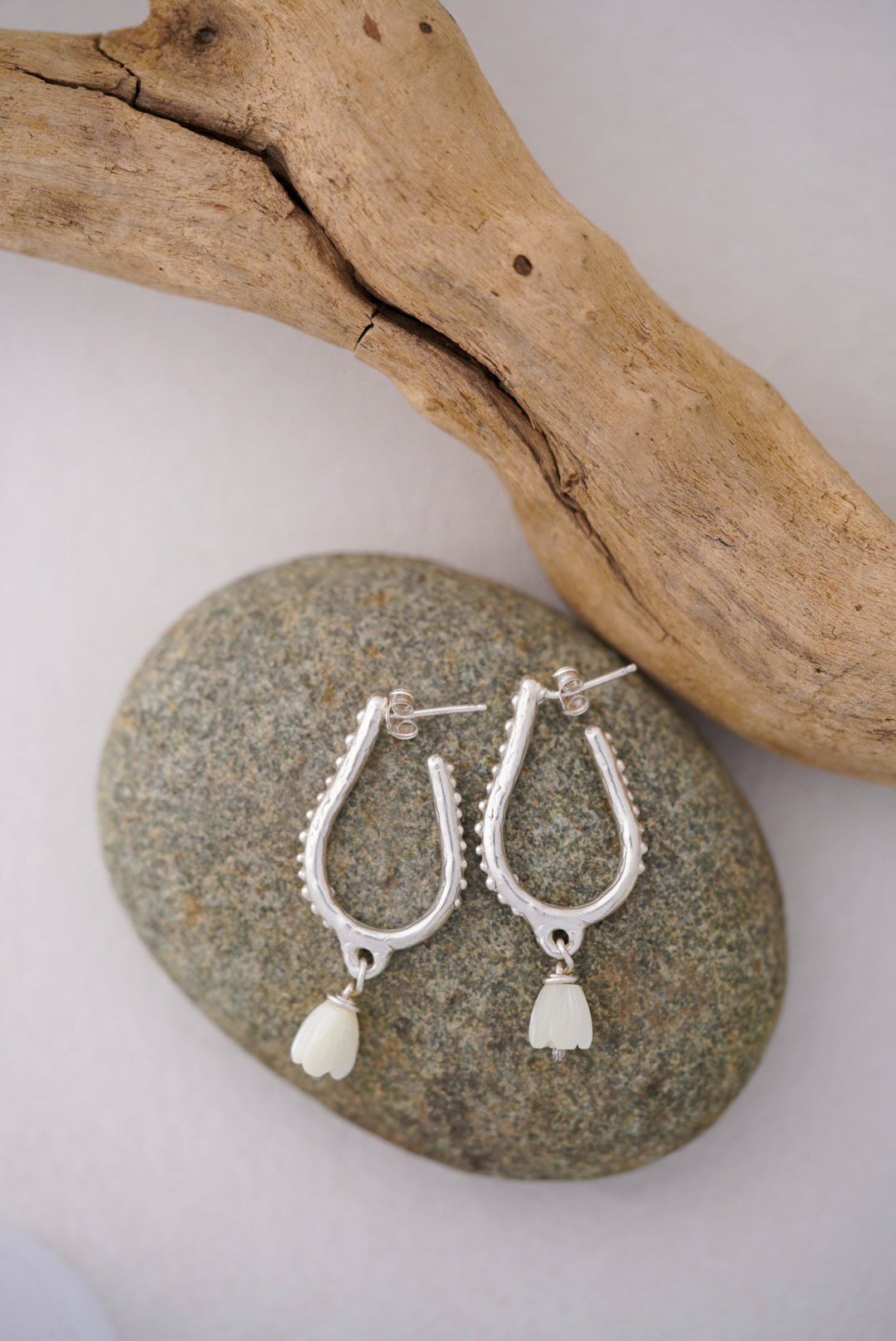 Silver earrings with white pearls on a stone surface with driftwood