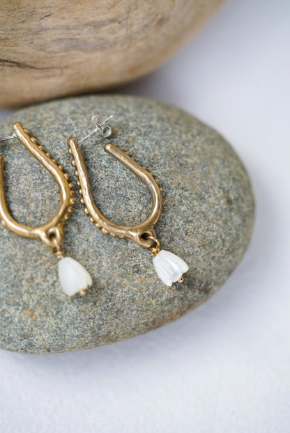 Gold earrings with peals on a stone surface