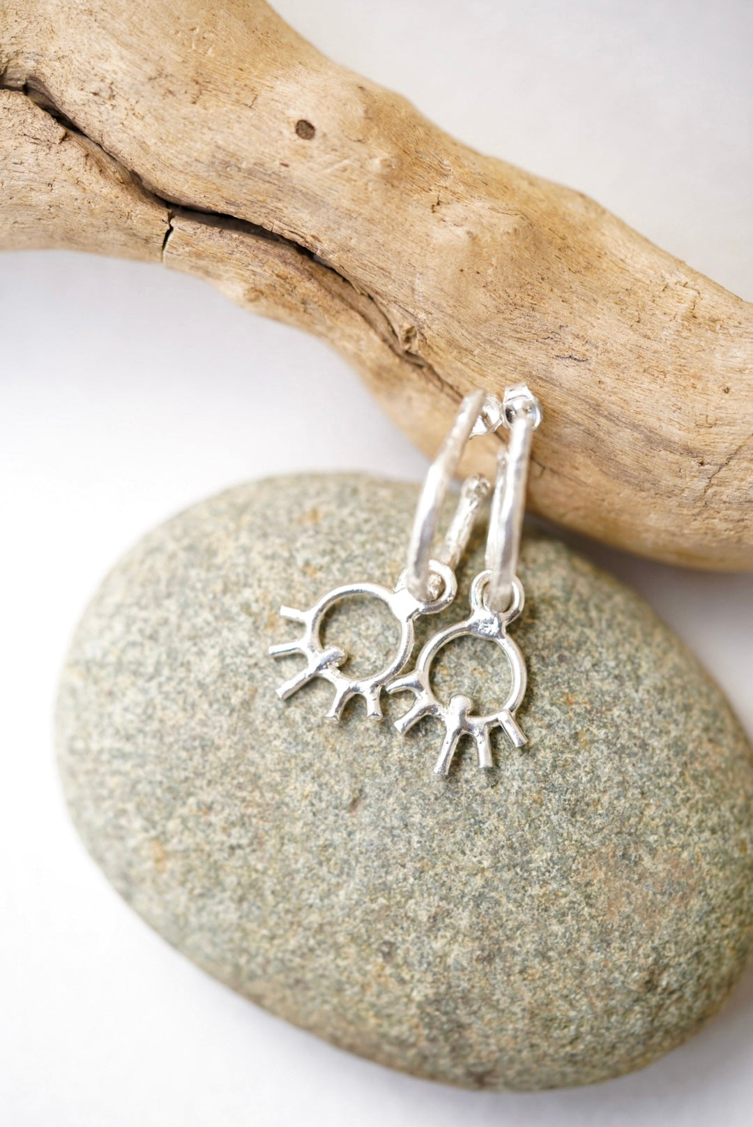Silver earrings with sun design on a stone and driftwood background
