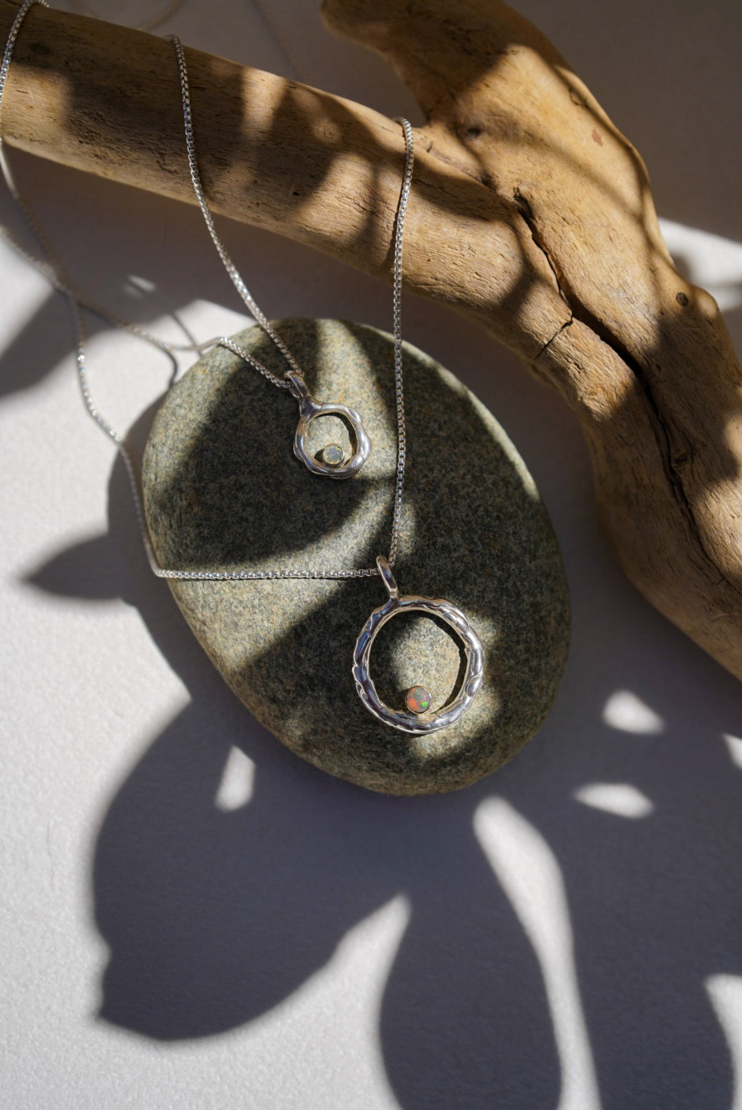 Silver pendant on a chain resting on a stone with a wooden surface underneath.