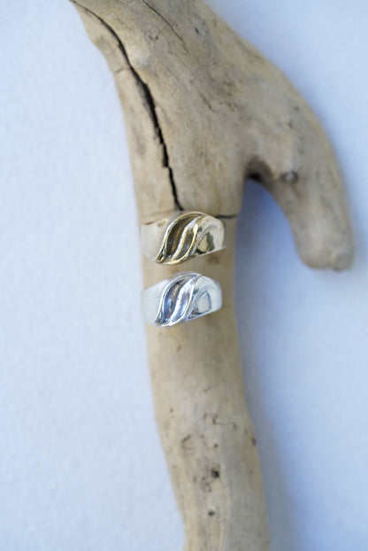 Two rings, one bronze and one silver, on a piece of driftwood against a white background.