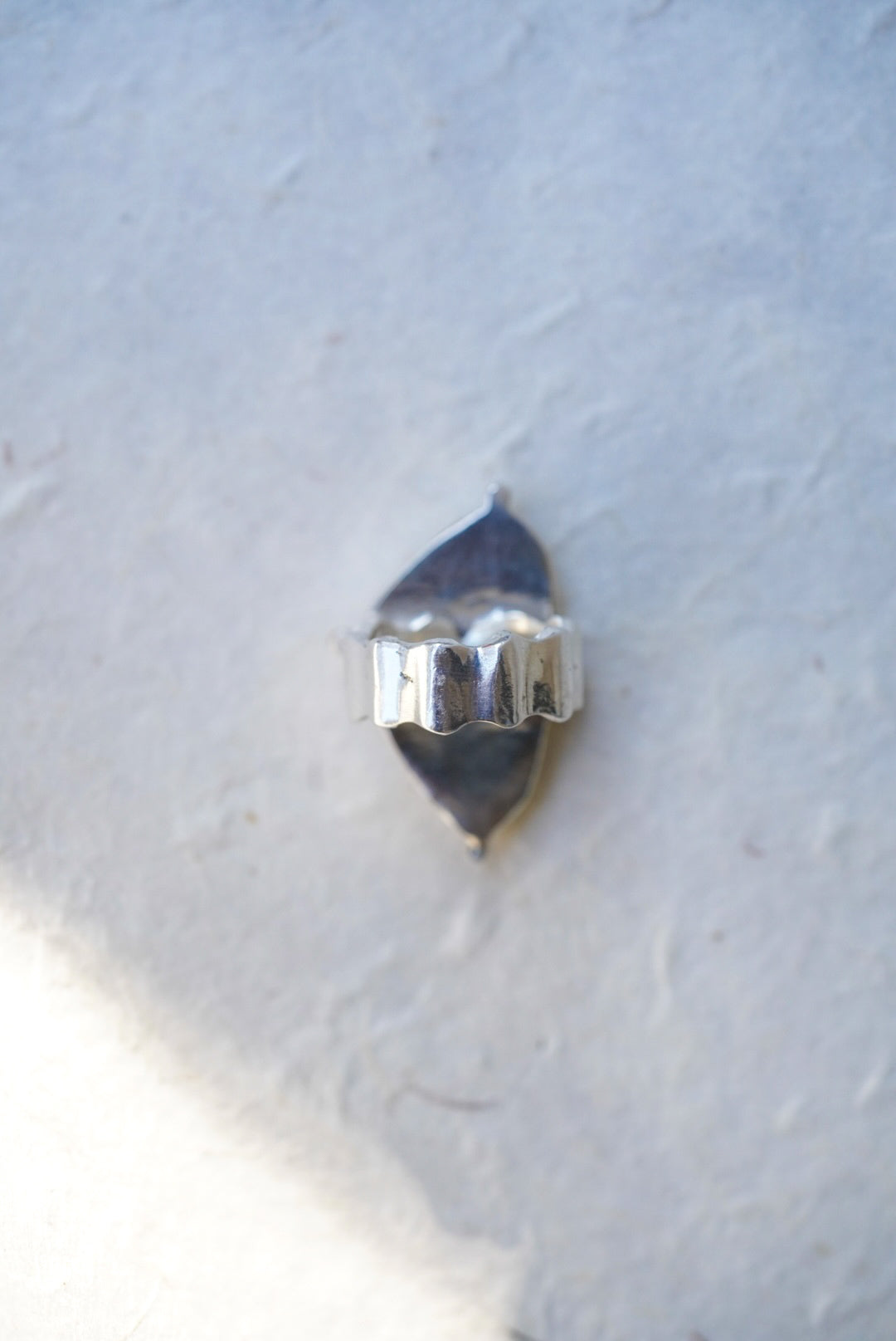 A silver ring with a textured, scalloped band,  against a light gray textured background.