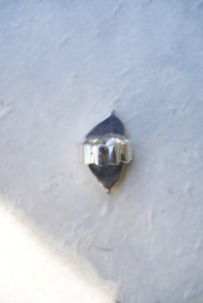 A silver ring with a textured, scalloped band,  against a light gray textured background.