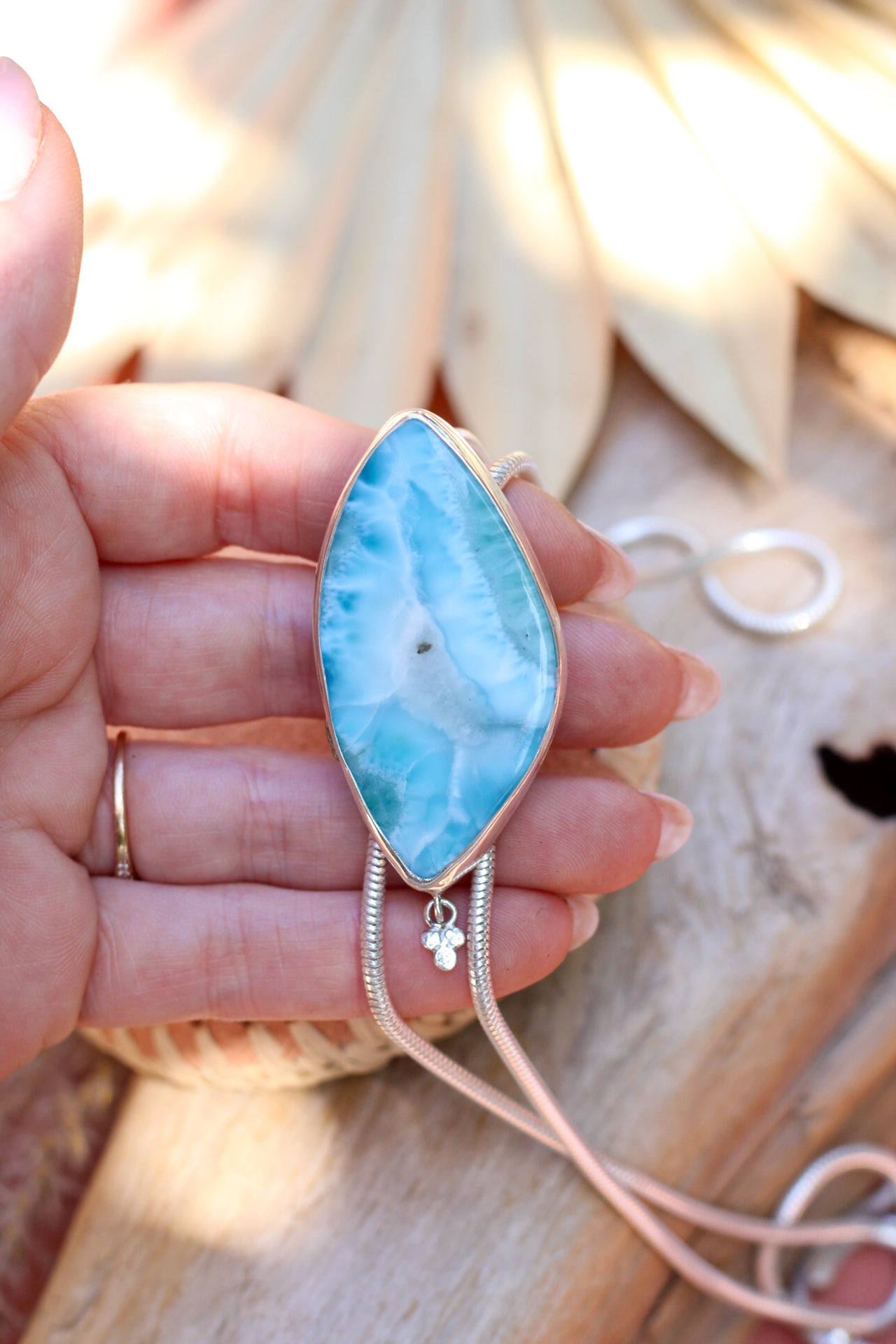 Teardrop-shaped blue stone pendant on a chain held by a hand with a blurred natural background