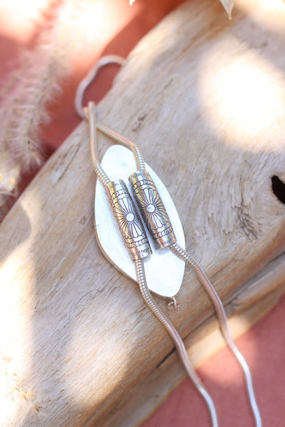 The back of a silver bolo necklace with a unique design on a wood surface