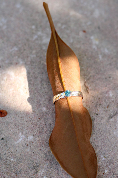 Gold ring with a blue-green gemstone on a brown leaf against a concrete background