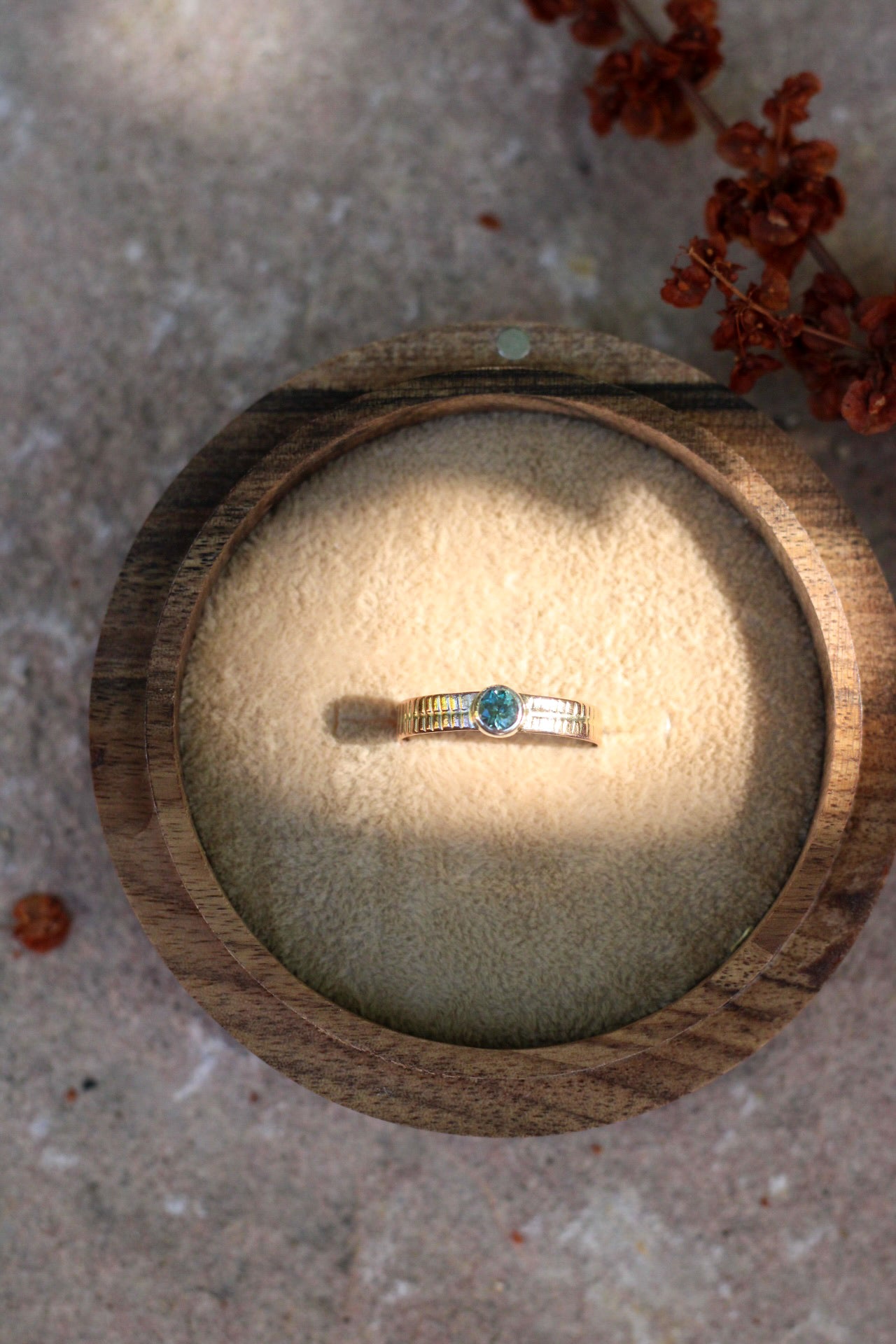 Gold ring with a blue gemstone in a wooden box on a textured surface
