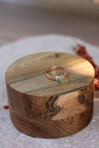 Gold ring with a blue-green gemstone on a wooden box