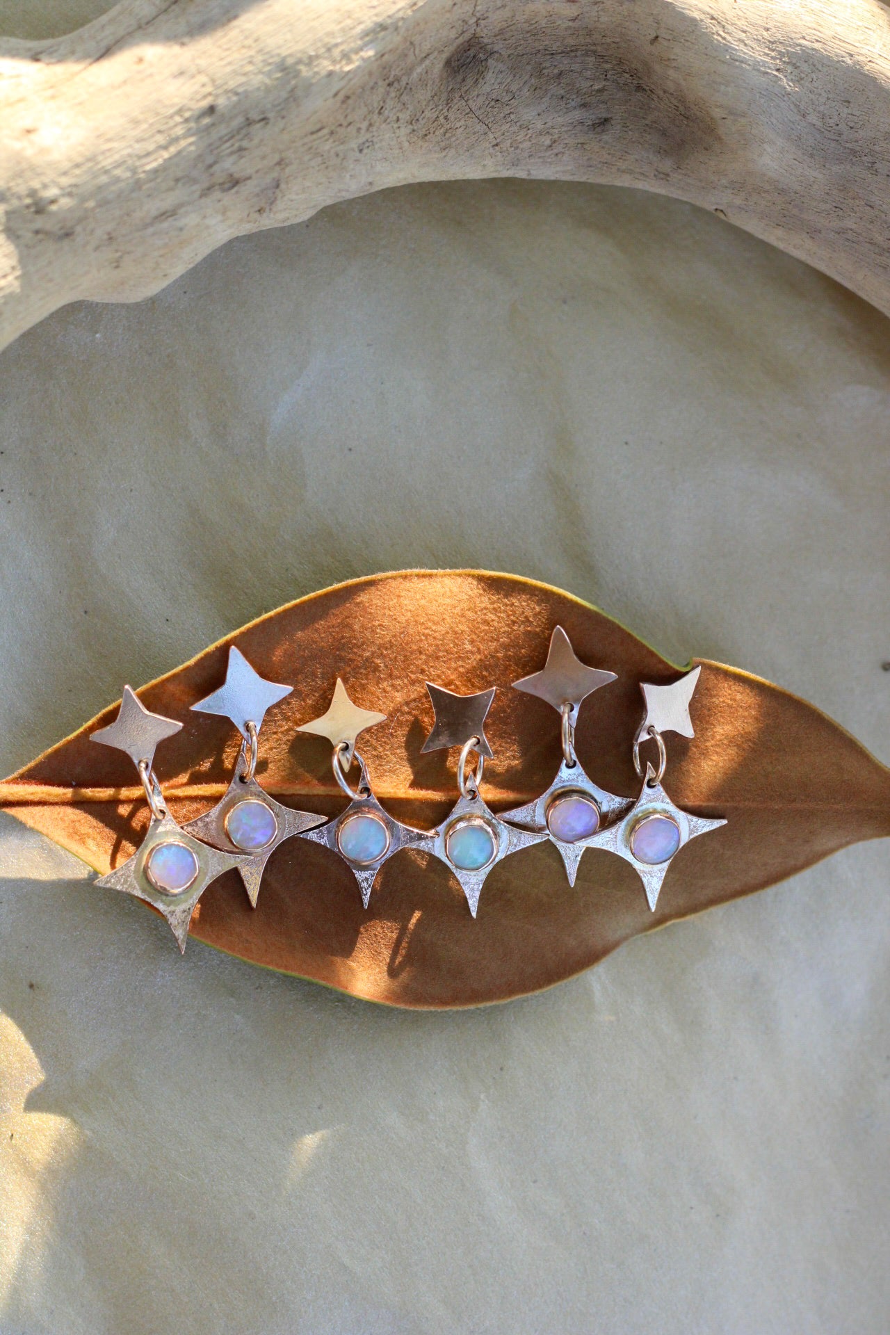 Star-shaped earrings with opals on a leaf-shaped stand against a stone background
