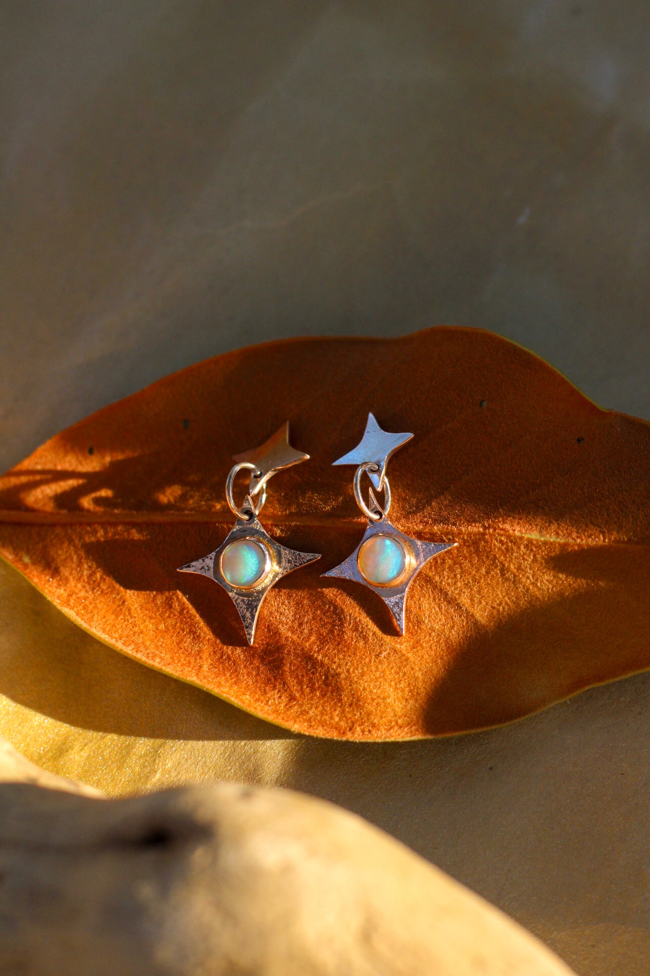 Pair of star-shaped earrings with opal stones on a brown leaf