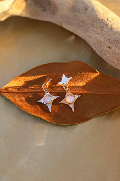 Star-shaped earrings with opals on a brown leaf with a natural background