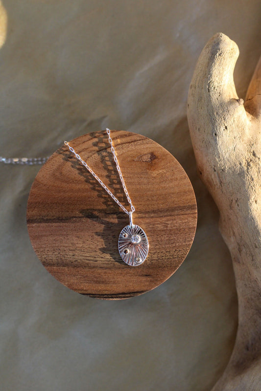 Silver necklace with a pendant that has a diamond and small gold accents, on a piece of wood.