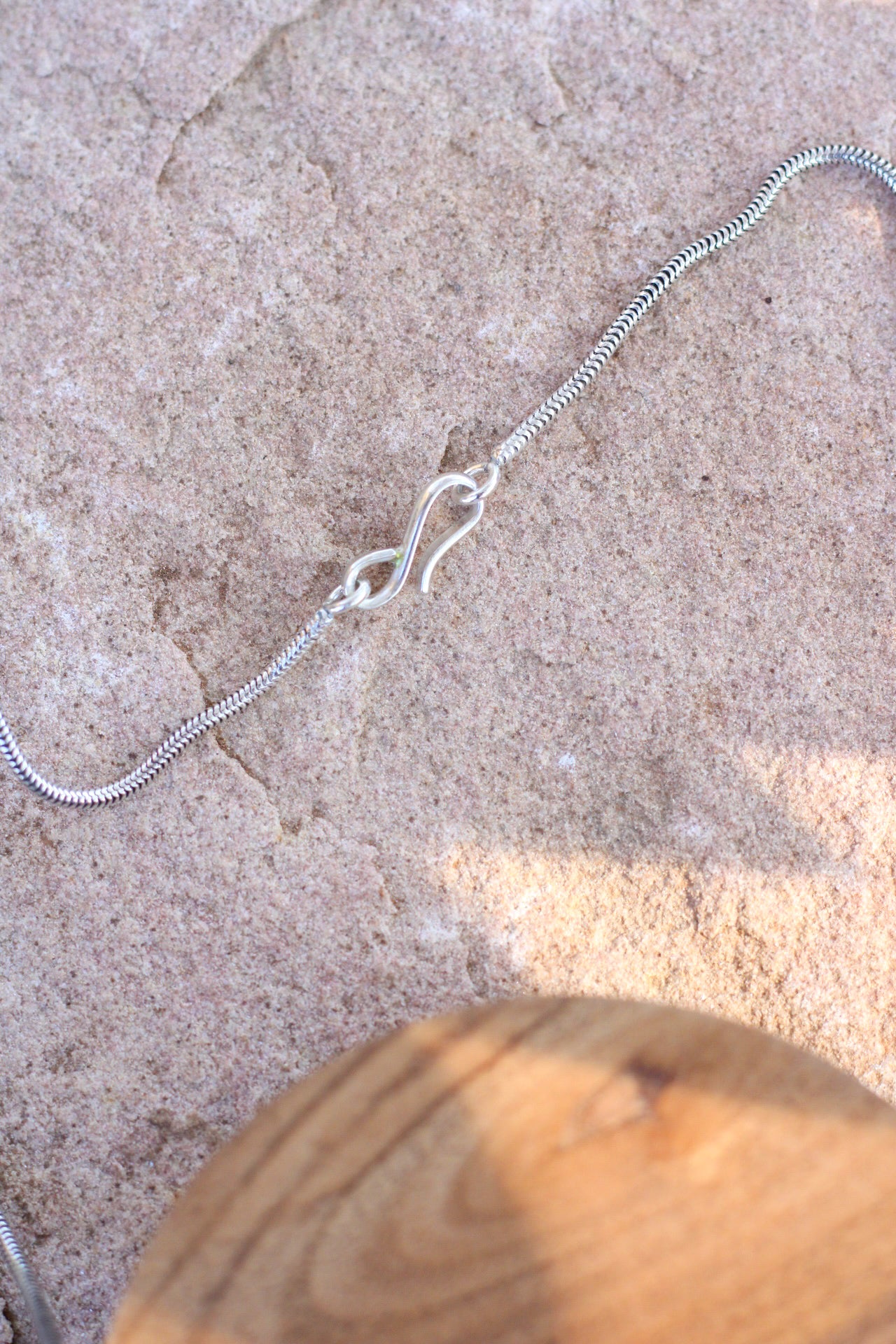 Silver chain clasp on a textured surface with a wooden object in the foreground