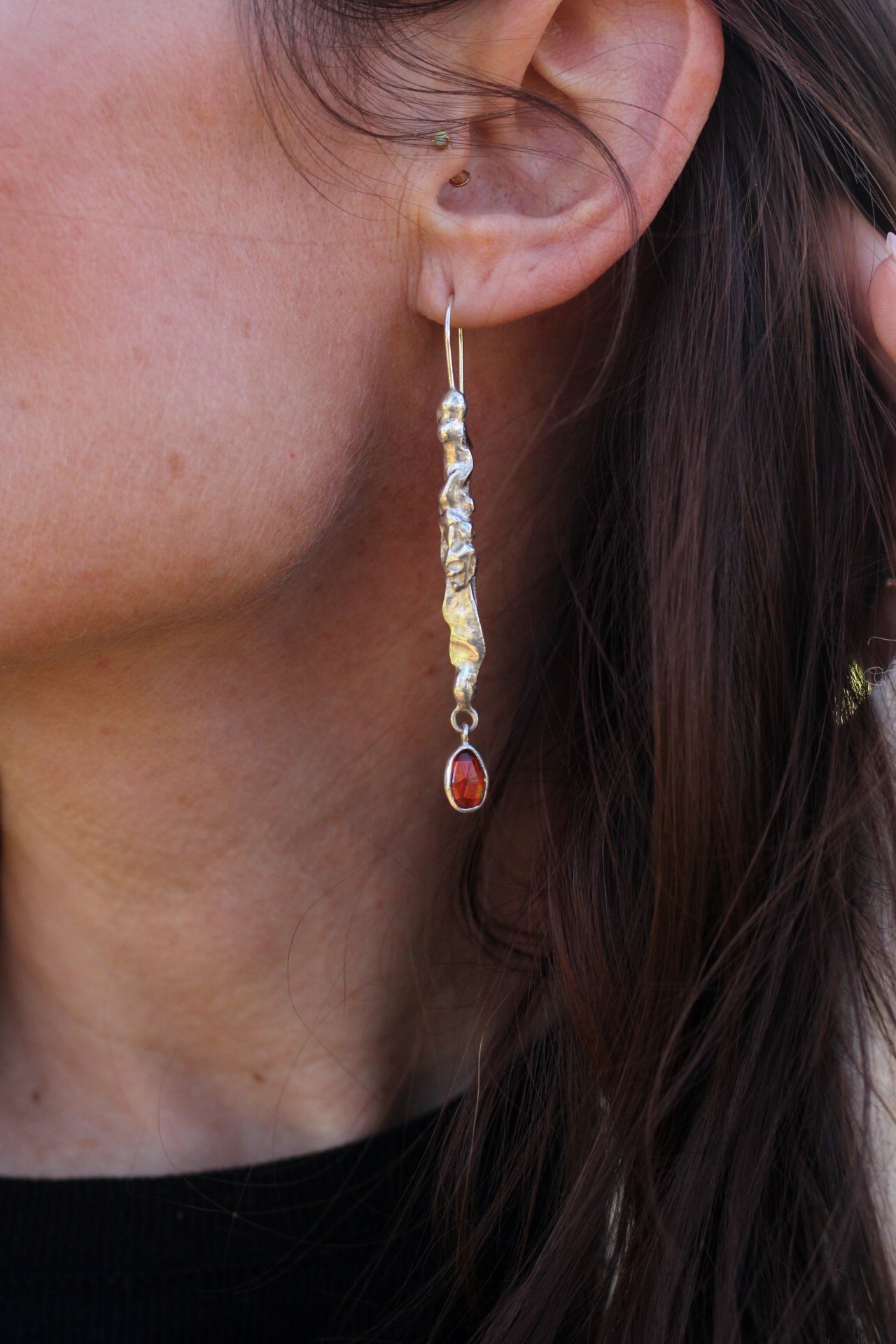 Close-up of a person wearing a silver earring and a red gemstone.