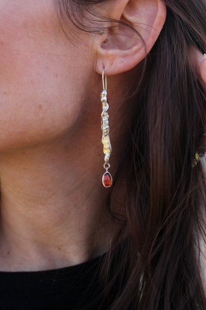 Close-up of a person wearing a silver earring and a red gemstone.