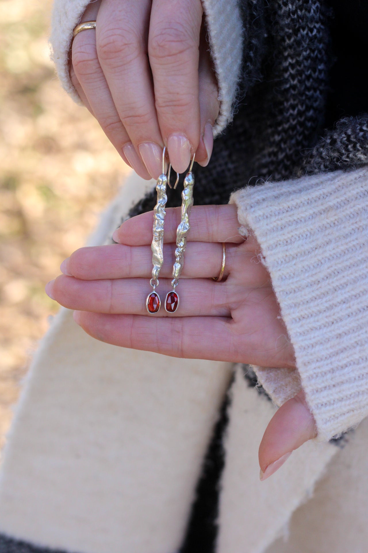 Close-up of hands holding a pair of earrings with red stones with a blurred natural background