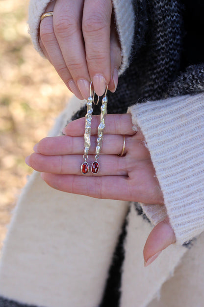 Close-up of hands holding a pair of earrings with red stones with a blurred natural background